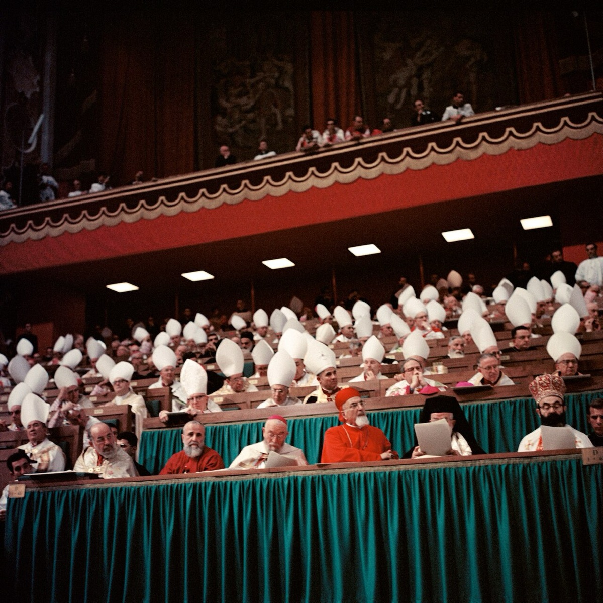 I padri conciliari seduti sulle tribune dell'aula, in mitra bianca; in prima fila i cardinali in rosso.
